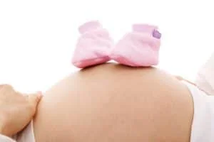 zwangere buik met twee roze schoentjes op de buik
