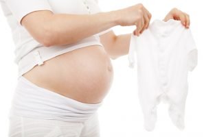 Een zwangere vrouw die haar buik en baby romper laat zien